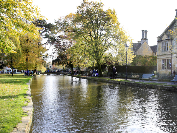 Image of River Windrush in Bourton town centre lined with trees and stone buildings.